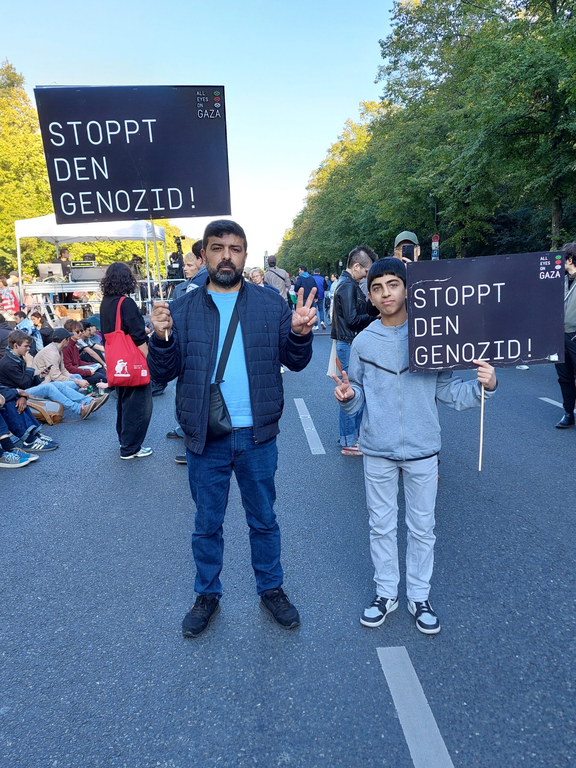 Wir sehen einen Vater mit seinem Sohn, beide ein Schild hochhaltend mit der Aufschrift "Stoppt den Genozid".