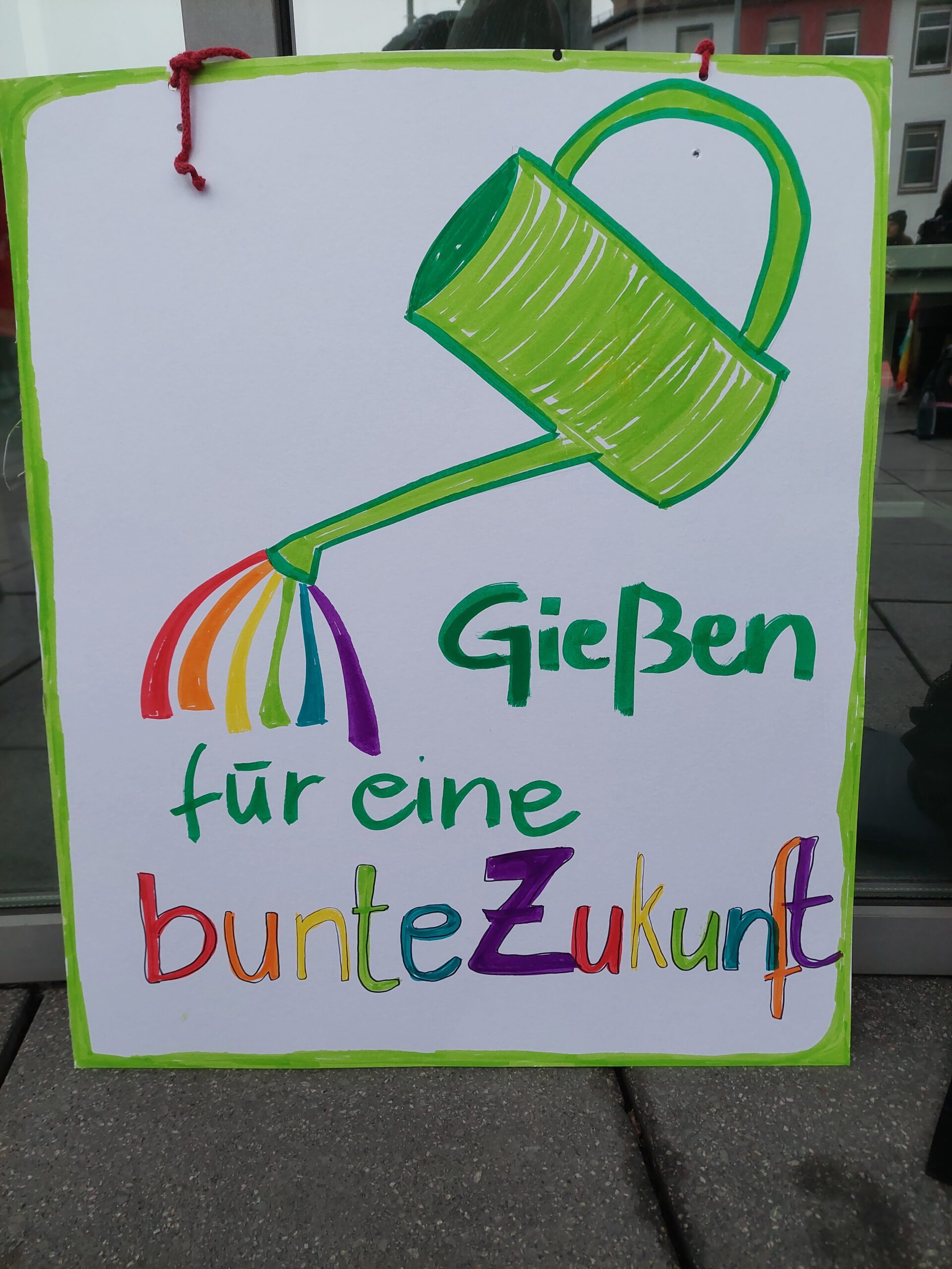 Auf dem Plakat ist eine Gießkanne zu sehen, die den folgenden Satz begießt: "Gießen für eine bunte Zukunft."