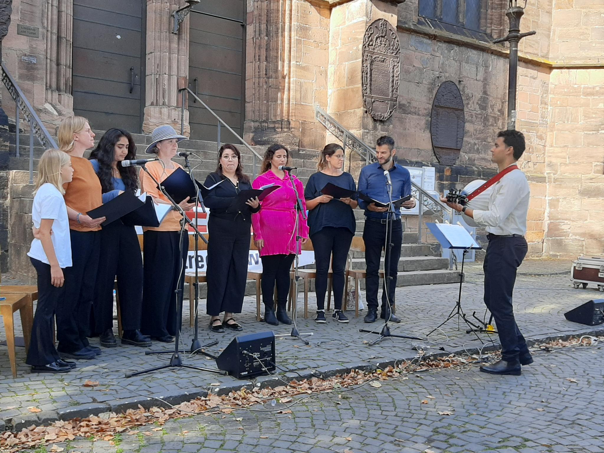 Wir sehen den Arabischen Chor Marburg mit seinem Leiter Faleh Khalessi vor der Lutherischen Pfarrkirche.